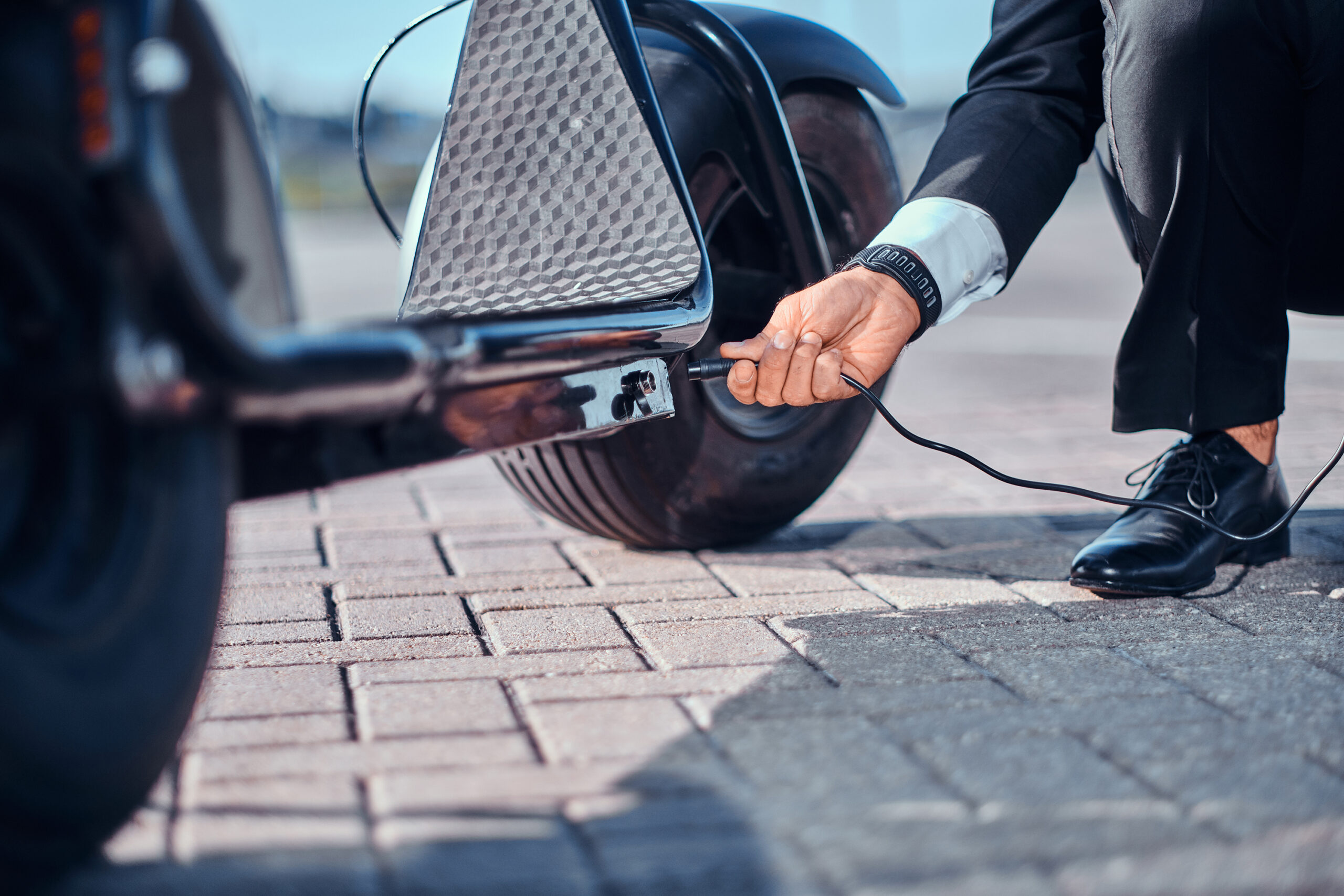 Elegant man is charging his electrical scooter with charger on special parking.